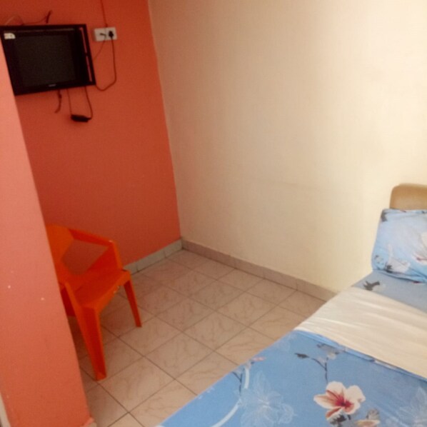 A small room with a bed, a chair, and a television mounted on the wall. - Relax Safari Hotel (Nairobi)