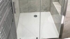 Cabina de ducha con paredes de vidrio, suelo de azulejos y barra de apoyo metálica.