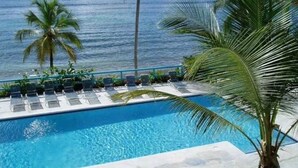 Una piscina con lettini e palme, con vista sull'oceano.