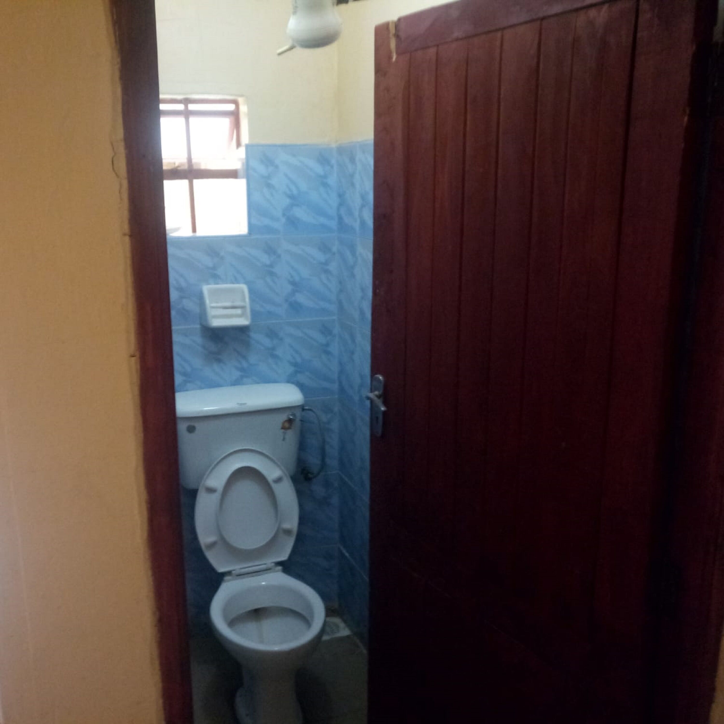 A small bathroom with a toilet, a hand dryer, and a window.