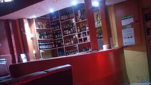 Un espace bar avec des étagères remplies de différentes bouteilles, un comptoir et un coin salon avec des chaises.