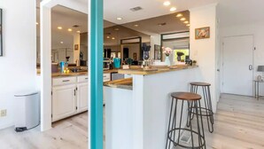 Cozinha moderna com armários brancos, parede em tom de verde-água e área de bar com banquetas.