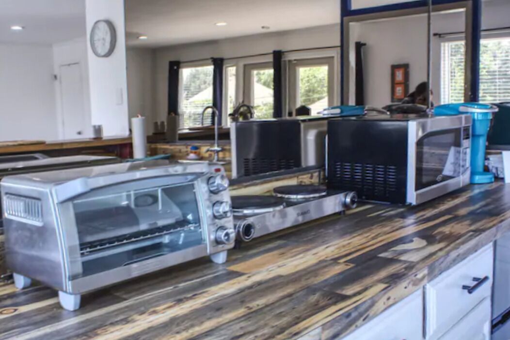 A kitchen with a stainless steel toaster oven, a commercial microwave, and a coffee machine on a wooden countertop.