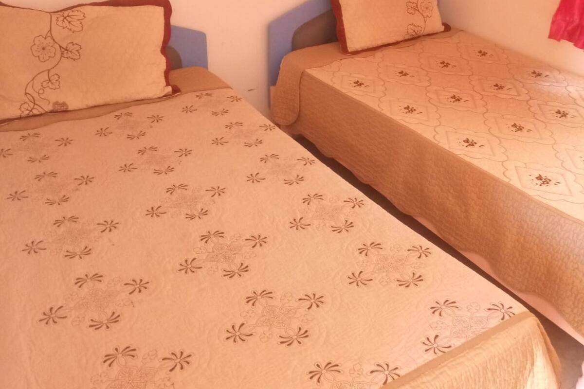 Zwei Einzelbetten mit blumigem Bettzeug in einem Zimmer mit schlichten Wänden.