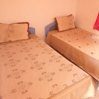Duas camas de solteiro com roupa de cama estampada em um quarto com paredes lisas.
