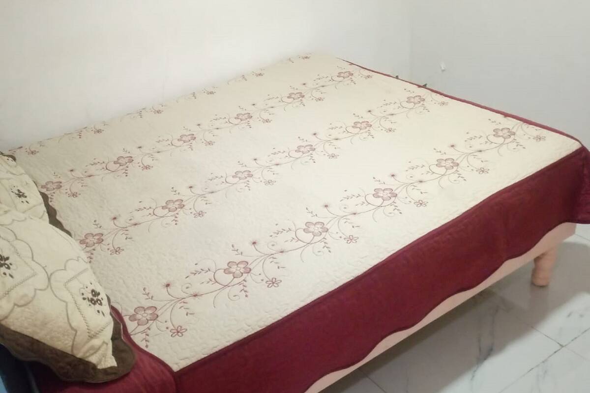 Ein kleines Zimmer mit einem Einzelbett, einer floralen Bettdecke und roten Akzenten.