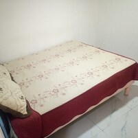Una habitación pequeña con cama individual, cubrecama estampado de flores y detalles en rojo.