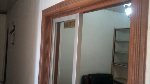 A reception area with a sign labeled "RECEPTION" on a door, a dark-colored sofa, and a wall-mounted shelf. - Serene Gates Guest House (Mai Mahiu)