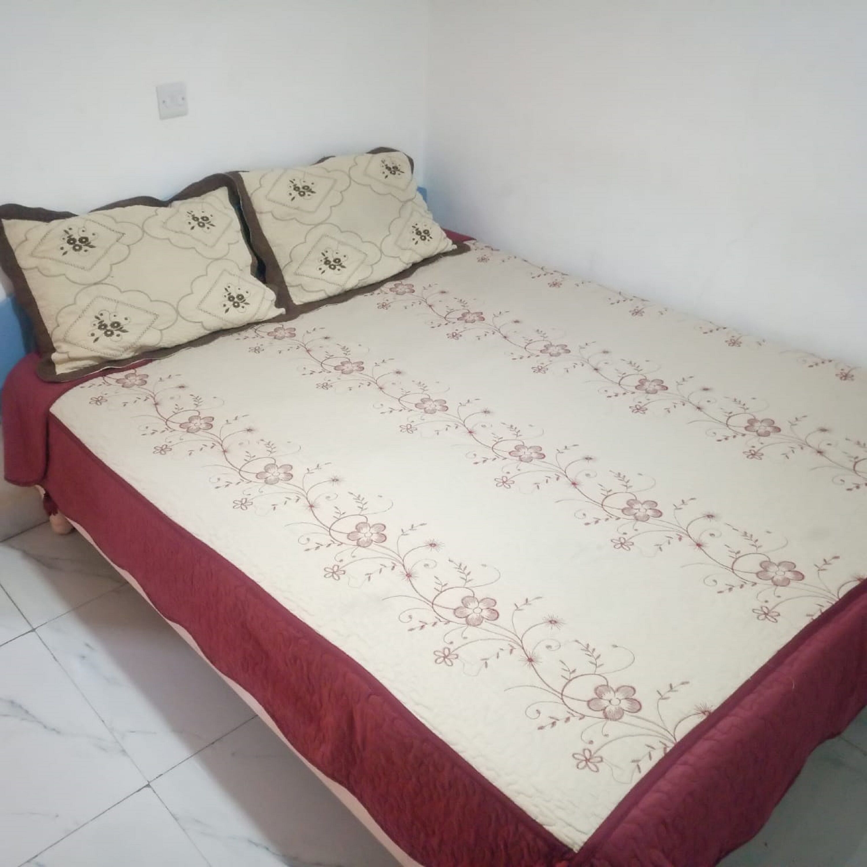 Uma cama pequena e bem arrumada, com colcha de padrão floral e dois travesseiros.