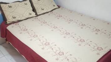 Uma cama pequena e bem arrumada, com colcha de padrão floral e dois travesseiros.