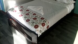 Un lit bien fait, avec une couvre-lit à motifs floraux et des oreillers blancs, une tête de lit en bois et une petite table de chevet sur laquelle se trouve une bouteille.