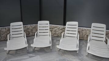 Vier witte lounge fauteuils staan op een rij tegen een stenen muur met een betegelde vloer.