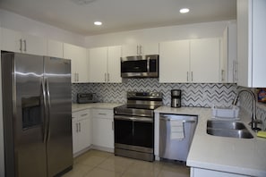 A modern kitchen with stainless steel appliances, white cabinets, and a herringbone tile backsplash. - Your Home away from home (Miami)