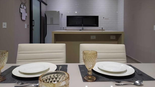 A modern dining area with a table set for two, a kitchen in the background, and a flat-screen TV mounted above the counter.
