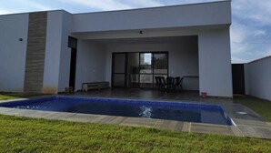 A modern house with a swimming pool, a patio with outdoor furniture, and a large sliding glass door leading to a covered area.