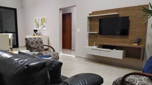 A modern living room with a black leather sofa, patterned armchairs, a wooden TV stand, and a flat-screen TV.