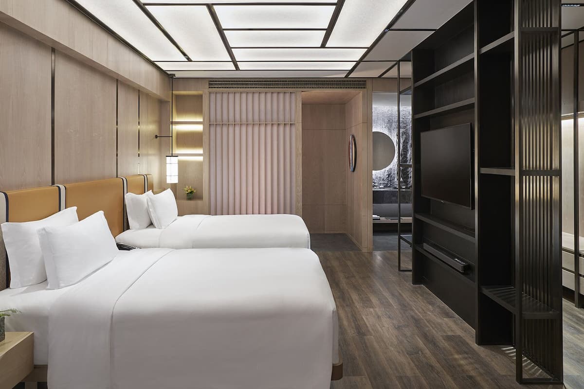 A hotel room with two beds, a TV, and a large window.