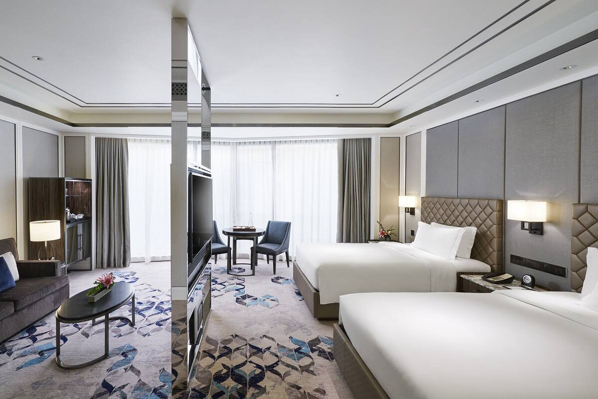 A hotel room with two beds, a desk, a chair, a TV, and a minibar.