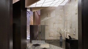 A modern lobby with a stone wall, a black vertical partition, a vase with flowers, and a reception desk. - Hotel Okura Manila at Newport World Resorts (Pasay)