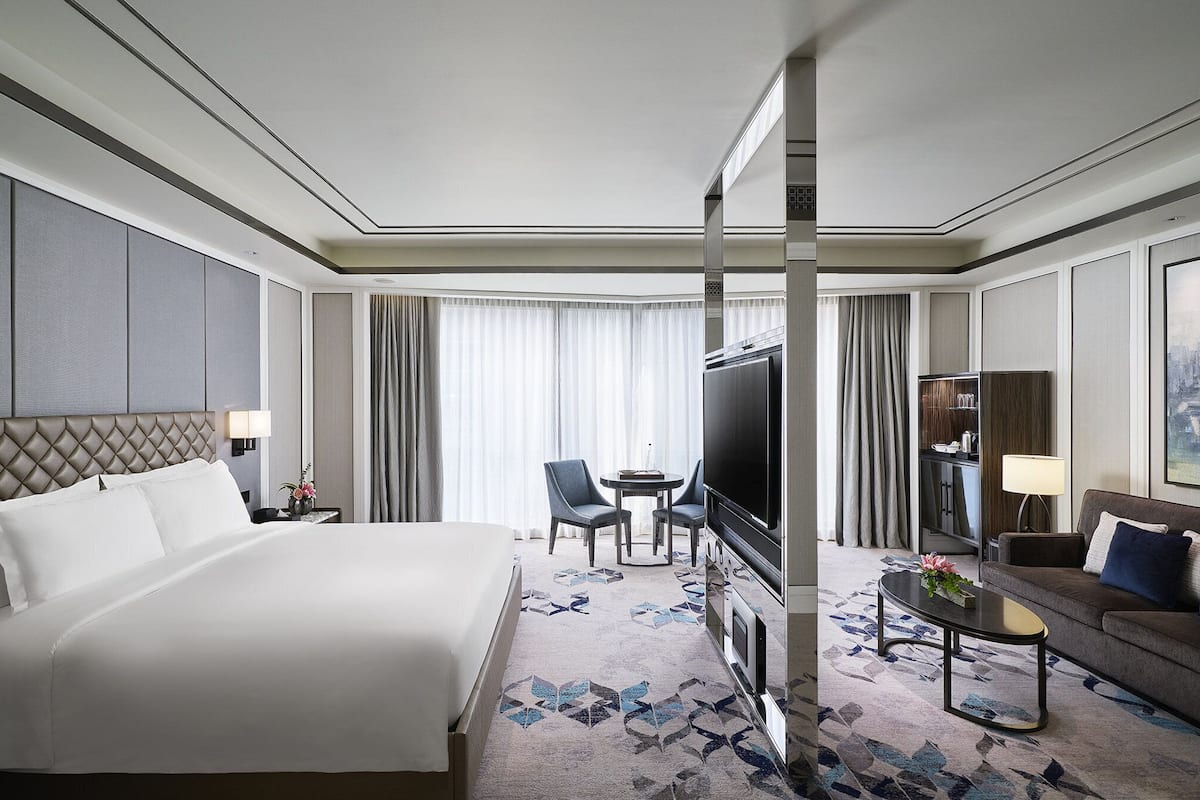 A hotel room with a large bed, a TV, a sofa, a coffee table, and a desk with a lamp.