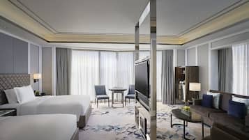 Habitación de hotel con dos camas, televisión, sofá, mesa de centro y una pequeña mesa con sillas.