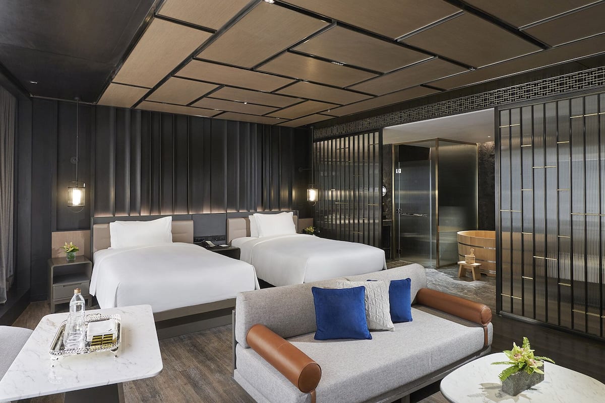 A hotel room with two beds, a sofa, a coffee table, and a sliding door to a bathroom.