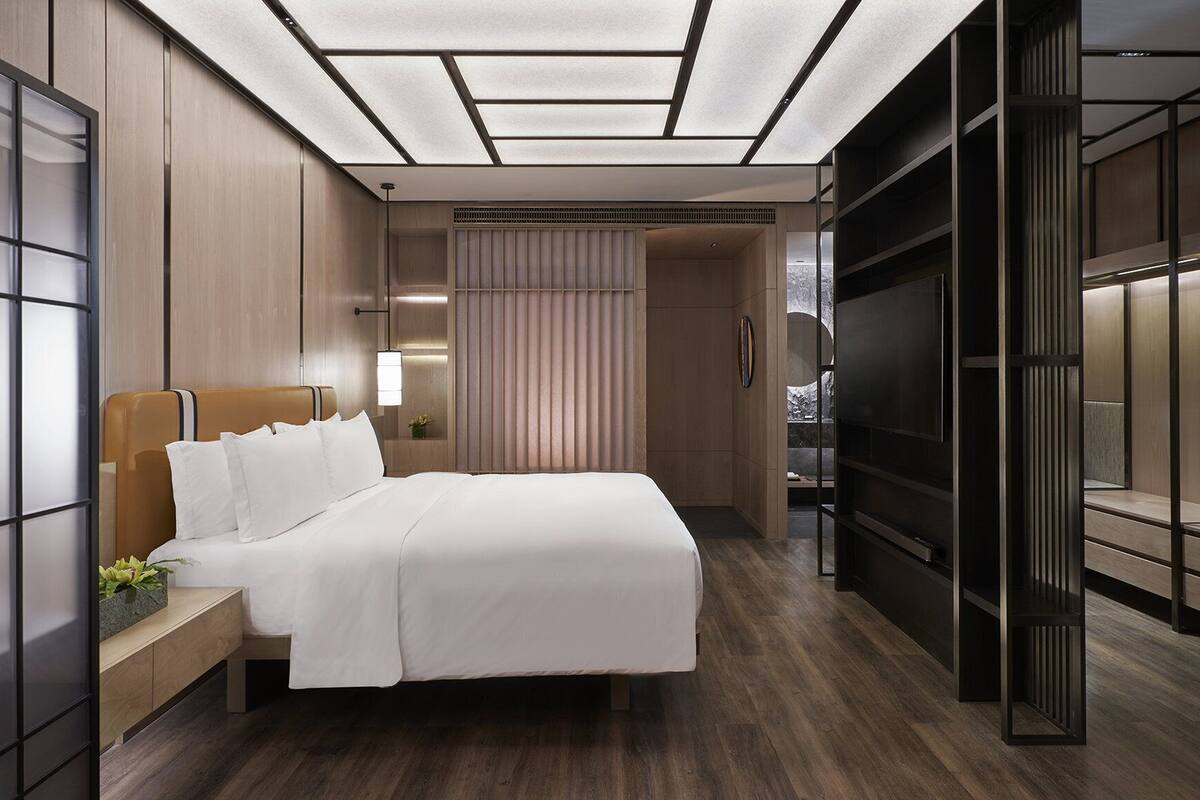 A modern hotel room with a large bed, bedside tables, a TV, and a sliding door leading to a bathroom.