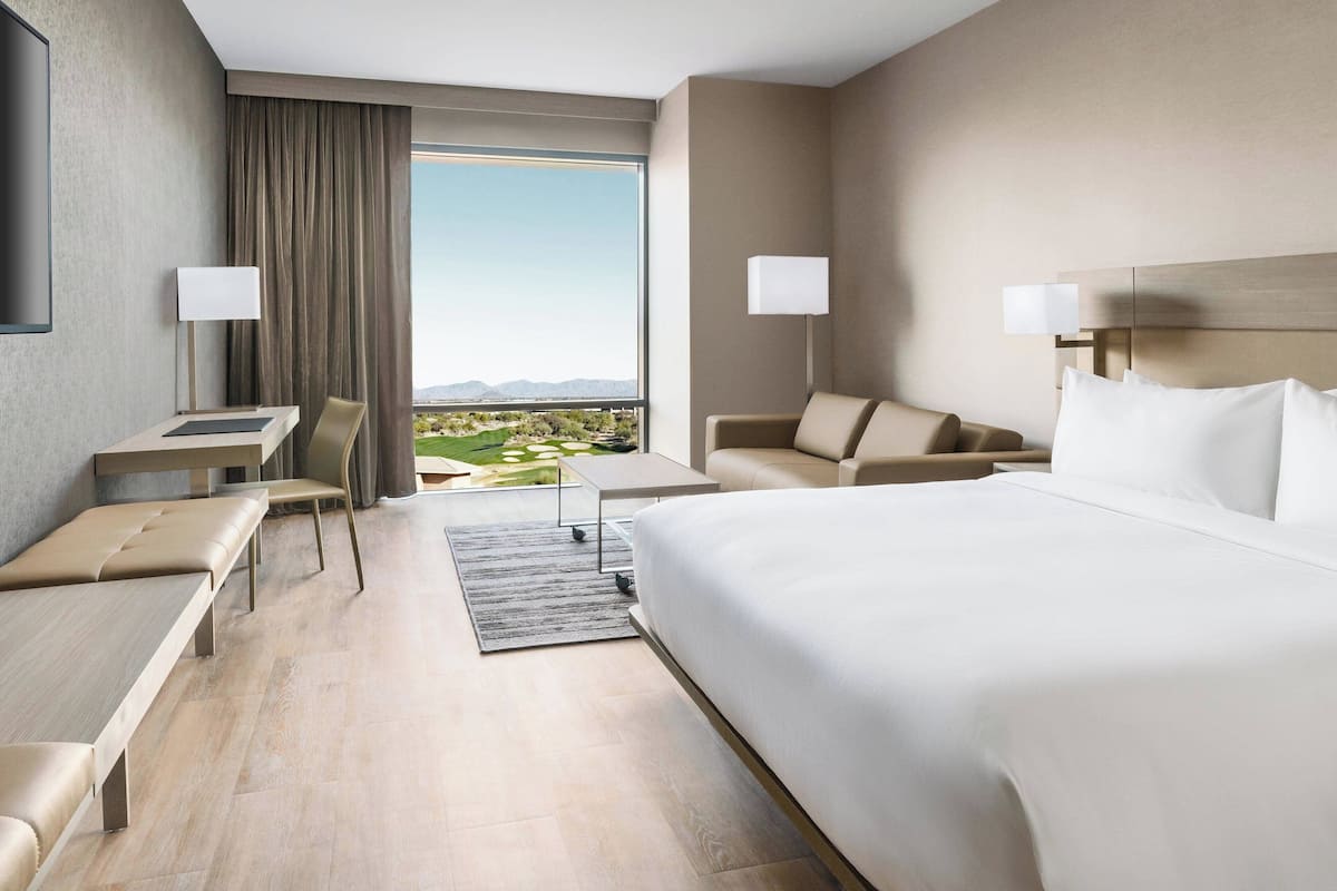 Een hotelkamer met een groot bed, een bureau, een stoel en een sofa. Er is uitzicht op het landschap door een groot raam.