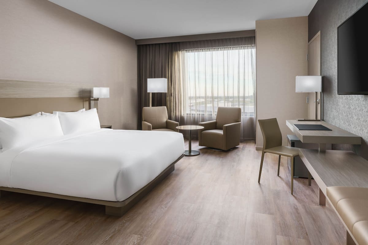 Een hotelkamer met een groot bed, twee fauteuils, een klein rond tafeltje, een bureau met stoel, en een aan de muur bevestigde televisie.
