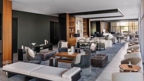 A modern hotel lobby with a long seating area, a reception desk, and large windows providing natural light.