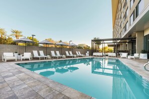Una piscina con sillas de descanso y sombrillas, rodeada por un muro de piedra y un edificio.