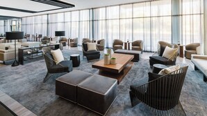 A spacious hotel lobby with modern furniture, large windows, and a flat-screen TV.