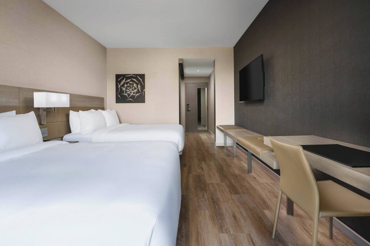 Een hotelkamer met twee bedden, een bureau, een stoel, een flatscreen televisie en een schilderij aan de muur.