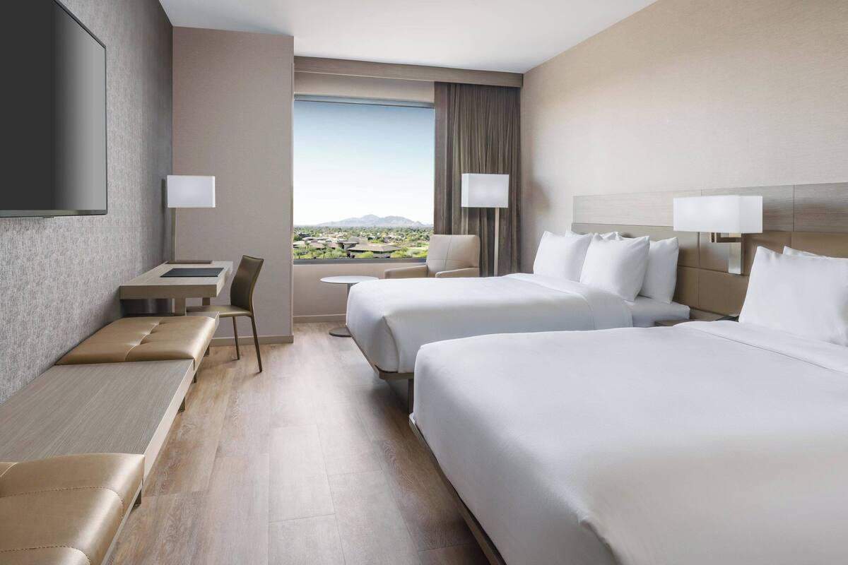 Een hotelkamer met twee bedden, een bureau, een stoel en een televisie.