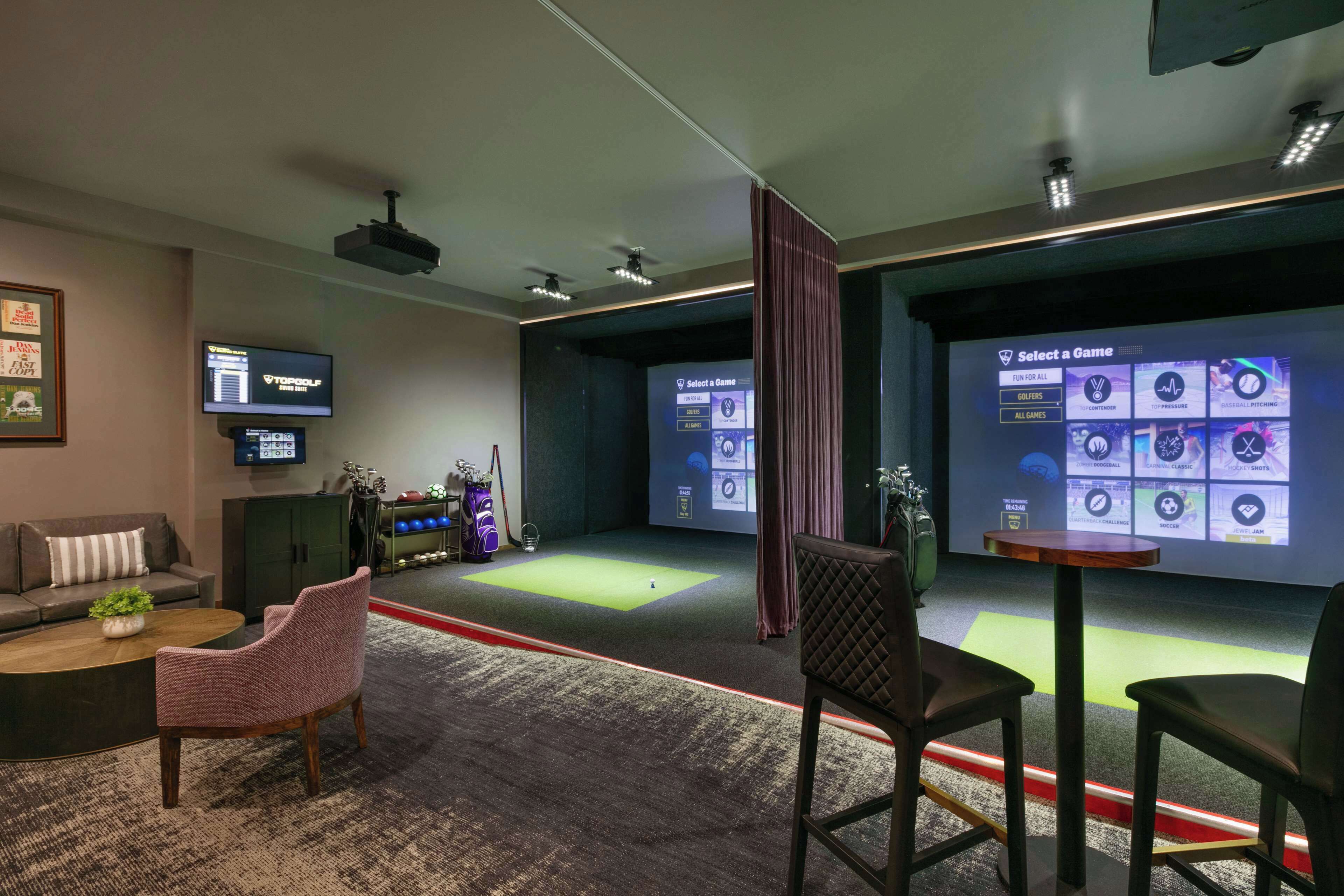 A room with a large screen displaying a game selection interface, a television, a billiards table, and seating arrangements.