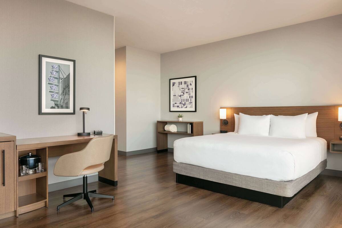 A hotel room with a bed, a desk, a chair, a nightstand, and two framed pictures on the walls.