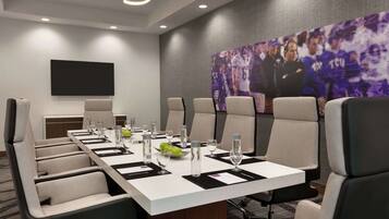 A conference room with a long table, multiple chairs, a flat-screen TV, and a large poster on the wall.