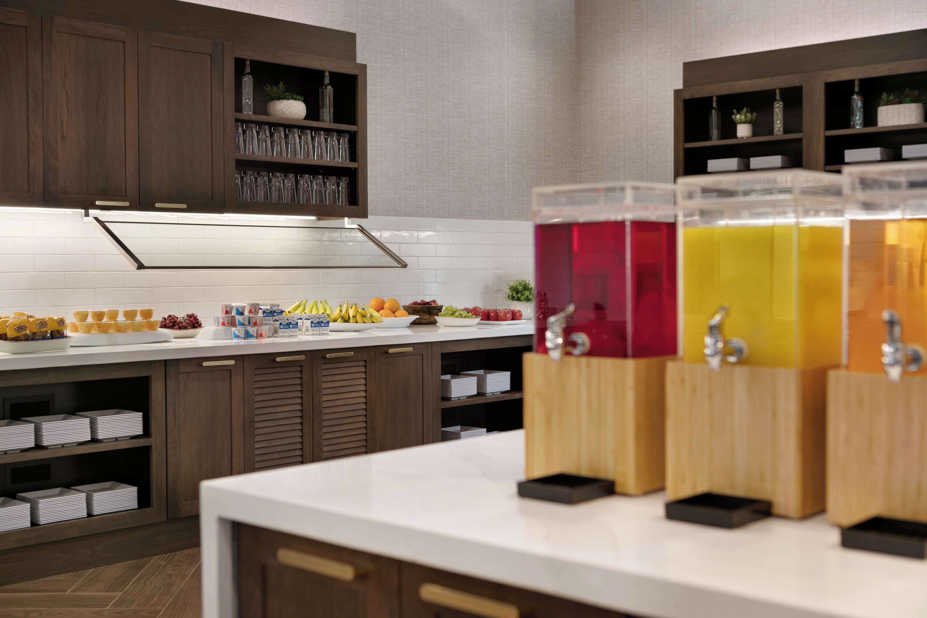 Una cocina moderna con encimera blanca, armarios de madera y un dispensador de bebidas con múltiples líquidos de colores.