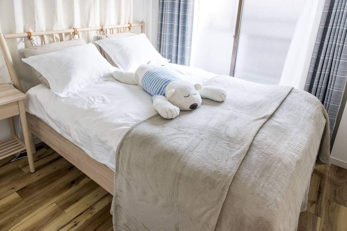 A bed with a white comforter and a teddy bear.