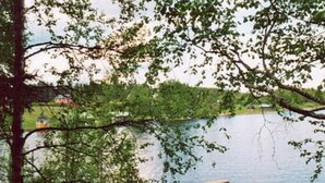 A lakeside view with a dock extending into the water, surrounded by trees and a distant building. - Raanumökki 4 by Interhome (Pello)