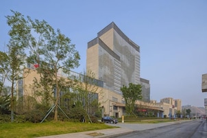 Un edificio moderno con un diseño de esquina llamativo, un área de estacionamiento y cielo despejado.
