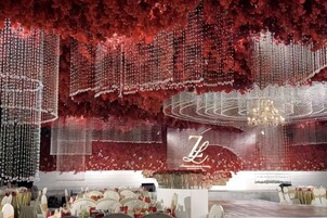 A banquet hall with a red floral backdrop, chandeliers, and a central stage.