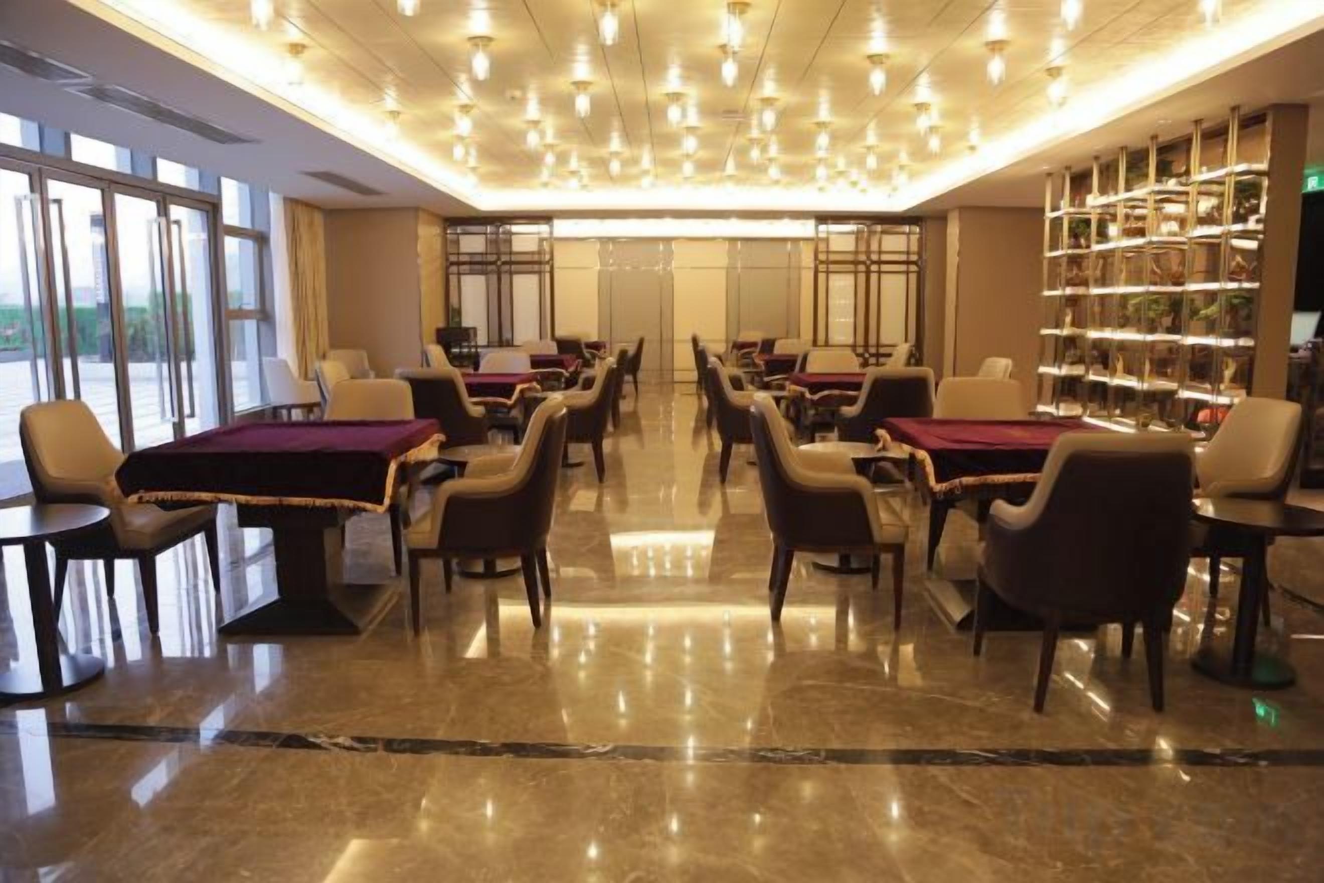 Un vestíbulo de hotel con varias mesas y sillas, suelo de mármol y una amplia estantería.