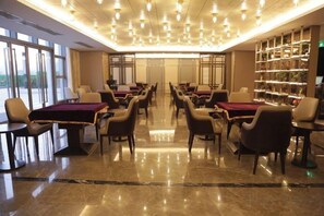 Un vestíbulo de hotel con varias mesas y sillas, suelo de mármol y una amplia estantería.
