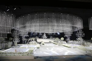 Un espacio para eventos formales con un escenario circular, asientos dispuestos y iluminación decorativa.