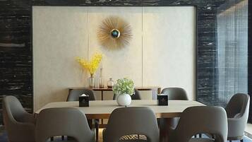 A modern dining area with a large table, six chairs, a decorative wall piece, and a vase with yellow flowers.