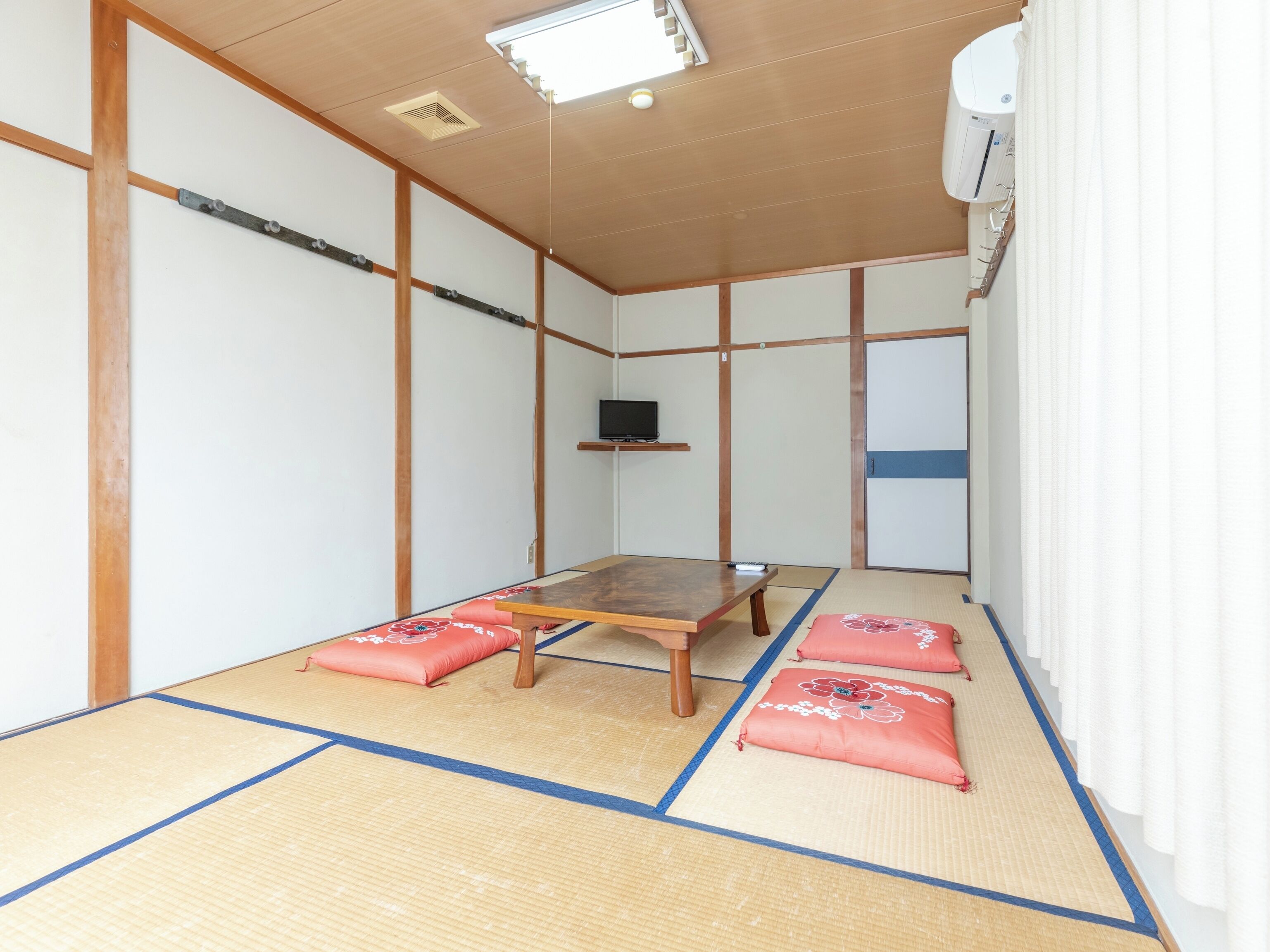Una habitación japonesa tradicional con suelo de tatami, una mesita baja, cojines, un televisor y un equipo de aire acondicionado.