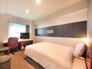 Habitación de hotel con cama, escritorio con televisor, silla y una pequeña mesa.
