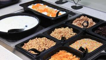 Un bufé con diversas opciones de comida, incluyendo un tazón grande de postre blanco, una bandeja de fruta naranja y varios recipientes con nueces y otros bocadillos.