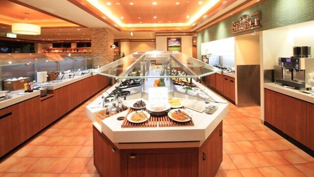 Uma área de buffet com um balcão central de serviço, vitrines de vidro e uma máquina de café.